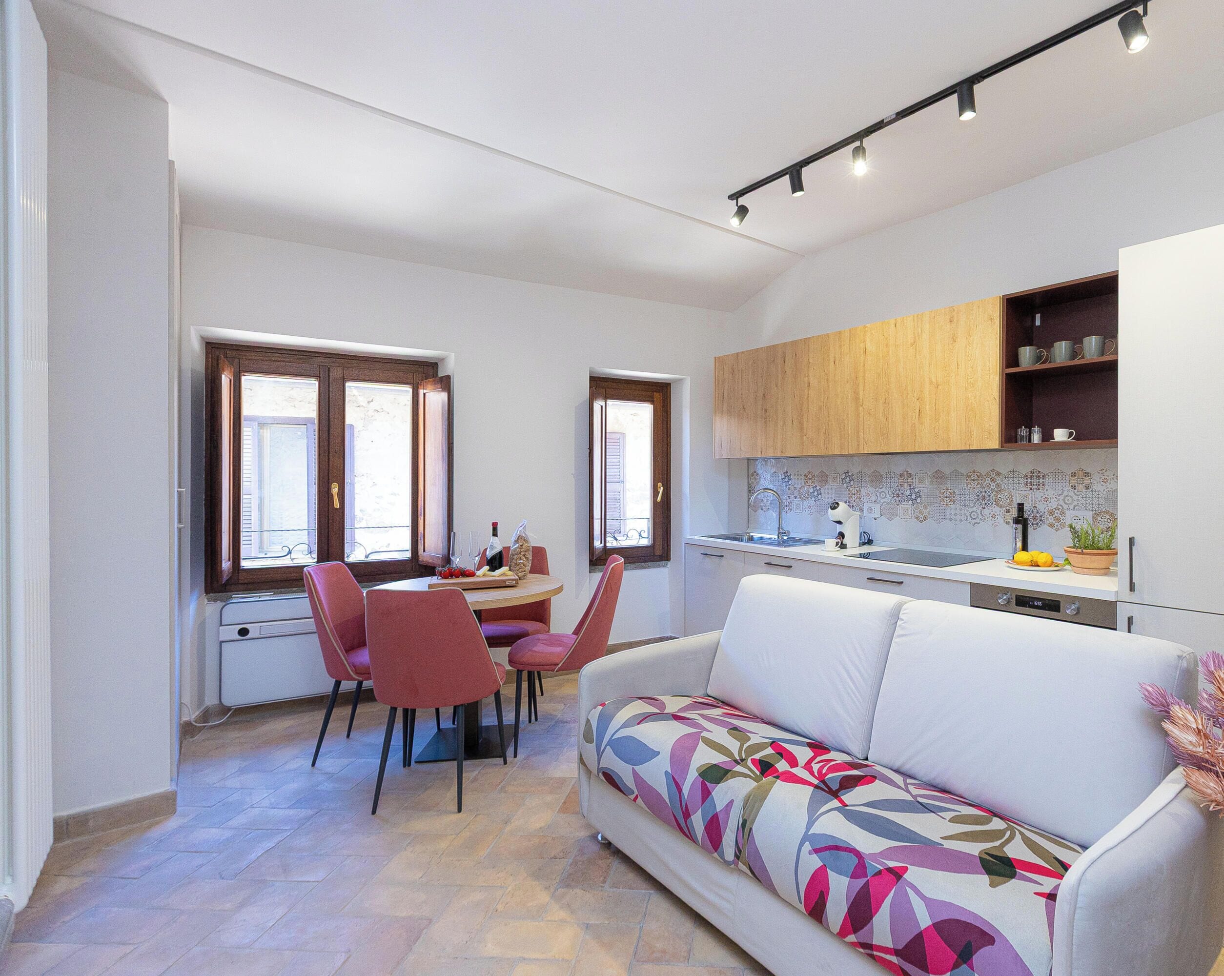 Una cocina moderna con horno empotrado, un comedor con mesa y sillas, y un sofá con un cojín de colores.