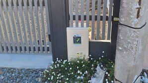 A gated entrance with a security keypad, a sign for 'Chambres-Hotels.fr,' and a small flower bed with white flowers. - Paloma by the Sea Guest Room with Shared Terrace, Garden, and Wi-Fi (Pornichet)