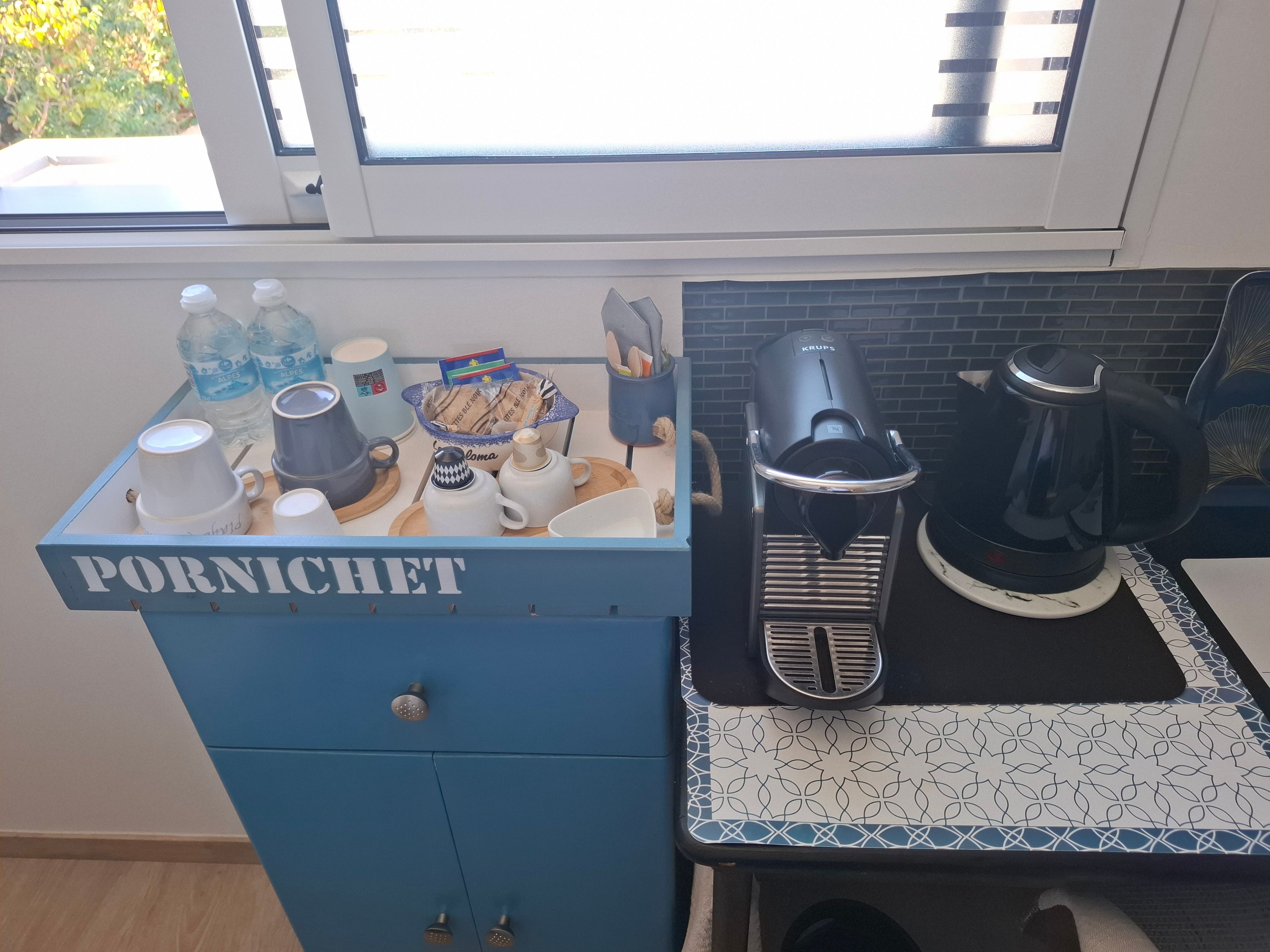 Un plan de travail de cuisine avec une machine à café, une bouilloire et un meuble bleu portant l’inscription « PORNICHET ».