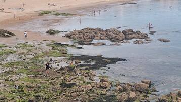 Een strand met rotsachtige delen, mensen en gebouwen op de achtergrond.