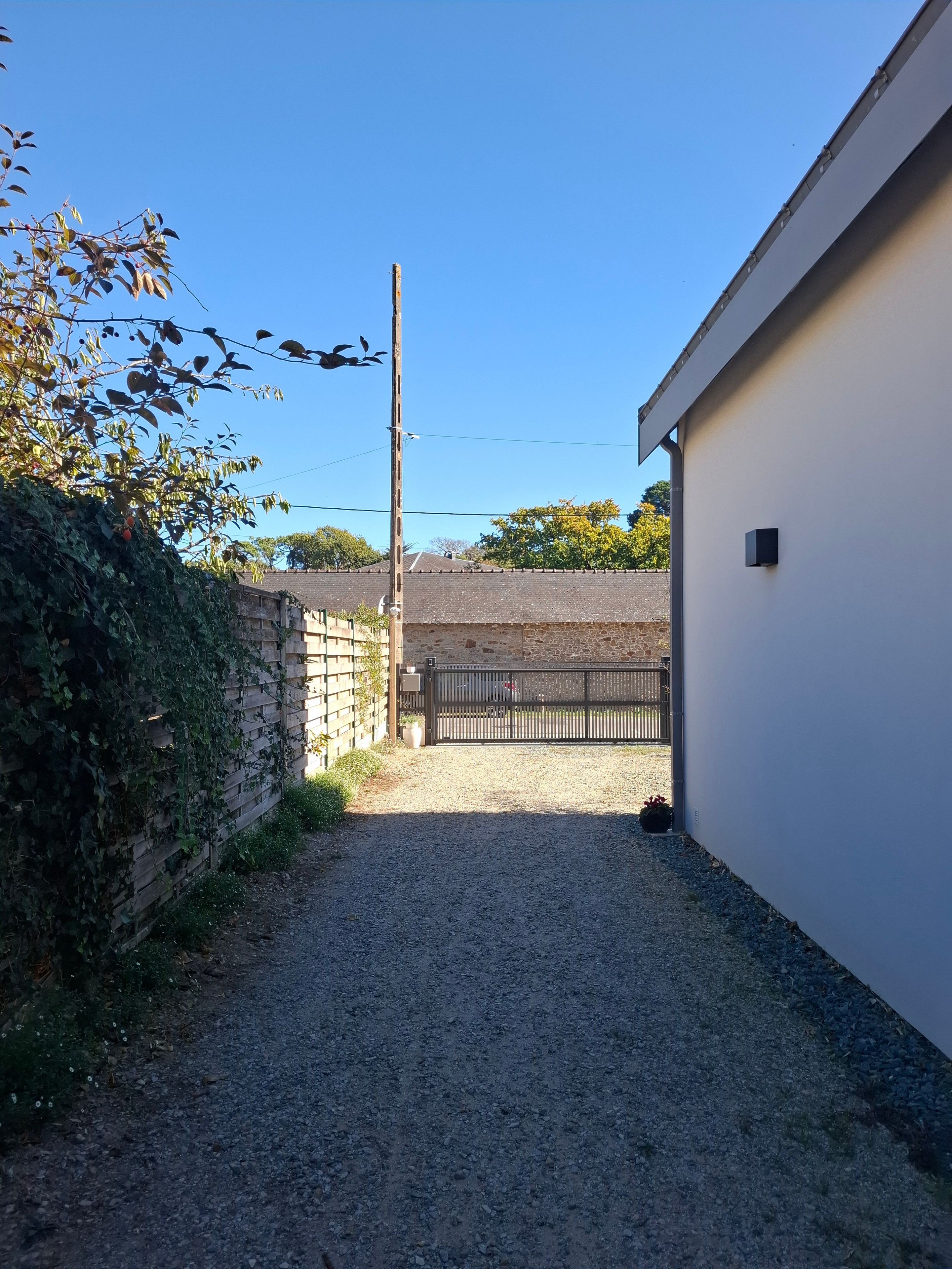 Ein Schotterweg führt zu einem befriedeten Bereich, einer Seite mit einer Steinmauer und der anderen Seite ein weißes Gebäude.