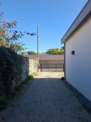 A gravel driveway leading to a gated area with a stone wall on one side and a white building on the other. - Guesthouse 'Paloma à la Mer' 150m from the beach with terrace, garden and Wi-Fi (Pornichet)