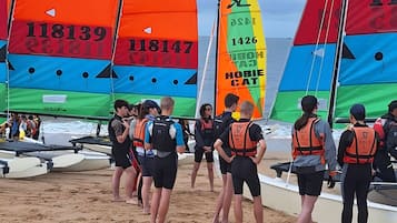 Uma praia com barcos à vela coloridos e pessoas usando coletes salva-vidas.