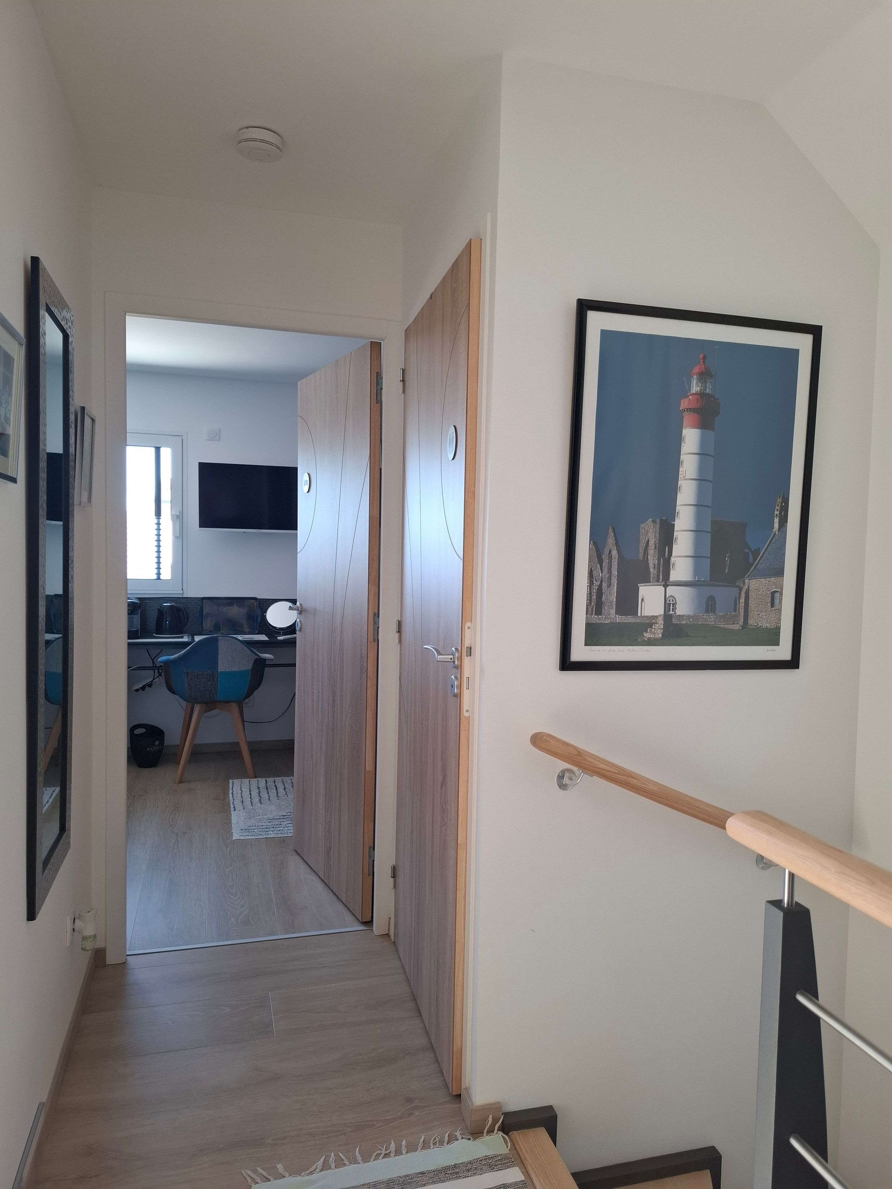 Ein Flur mit Holzboden, einer Holztreppe mit Geländer und einem gerahmten Bild eines Leuchtturms an der Wand.