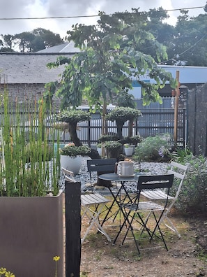 Un patio con tavolo e sedie, circondato da piante in vaso e un recinto in legno.