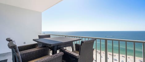 A balcony with wicker furniture overlooking a beach.