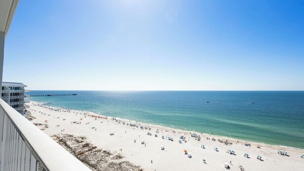 Ein Strand mit einem Steg, der sich ins Meer erstreckt, ein klarer Himmel und Meerblick vom Balkon.