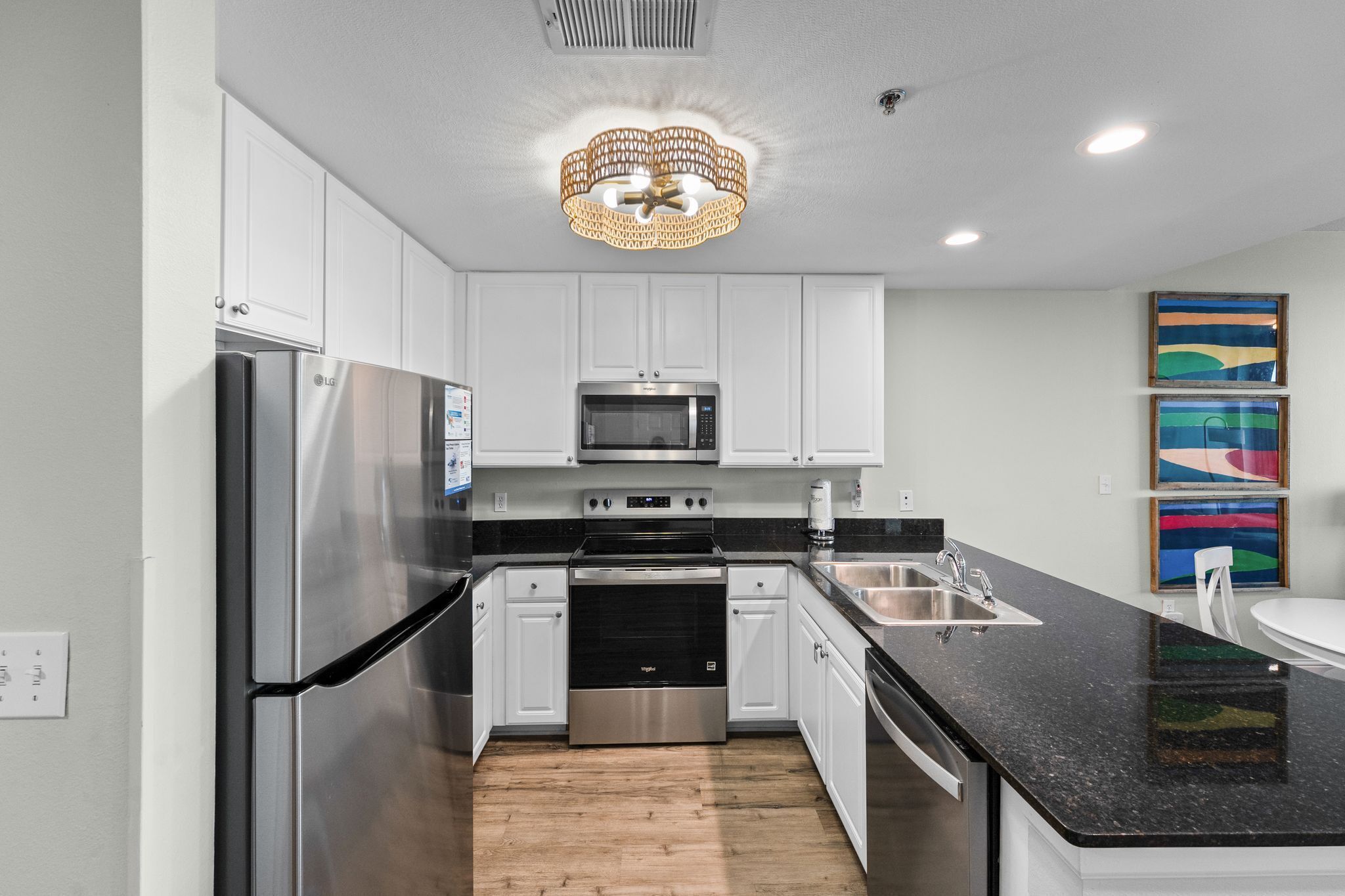 A modern kitchen with stainless steel appliances, white cabinetry, a black countertop, and a chandelier.