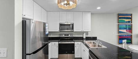 A modern kitchen with stainless steel appliances, white cabinetry, a black countertop, and a chandelier.