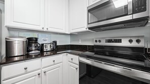 Eine moderne Küche mit weißen Schränken, einem Edelstahlkühlschrank, einer Kaffeemaschine, einem Toaster und einer Mikrowelle.