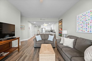 A living room with a sofa, a coffee table, and a TV on a wooden stand. - Lighthouse 1414 - Owner Managed, Fully Updated. Beautiful 3BR Gulf Front Condo. (Gulf Shores)