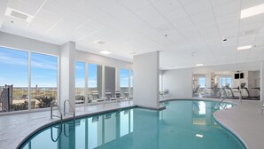 Ein Hallenbad mit großen Glaswänden, Blick auf die Stadt und Trainingsgeräten im Hintergrund.