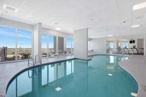 Ein Hallenbad mit großen Glaswänden, Blick auf die Stadt und Trainingsgeräten im Hintergrund.