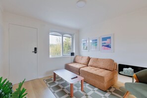Ein Wohnzimmer mit einer Couch, einem Couchtisch, einem Fernseher und einem Fenster mit Blick auf Bäume.