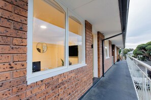 Ein Korridor mit Backsteinwand, großen Fenstern und einem Balkon mit weißen Geländern.