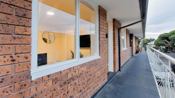 A corridor with a brick wall, large windows, and a balcony with white railings. - Stylish Brunswick Retreat Free Parking Near CBD (Brunswick)
