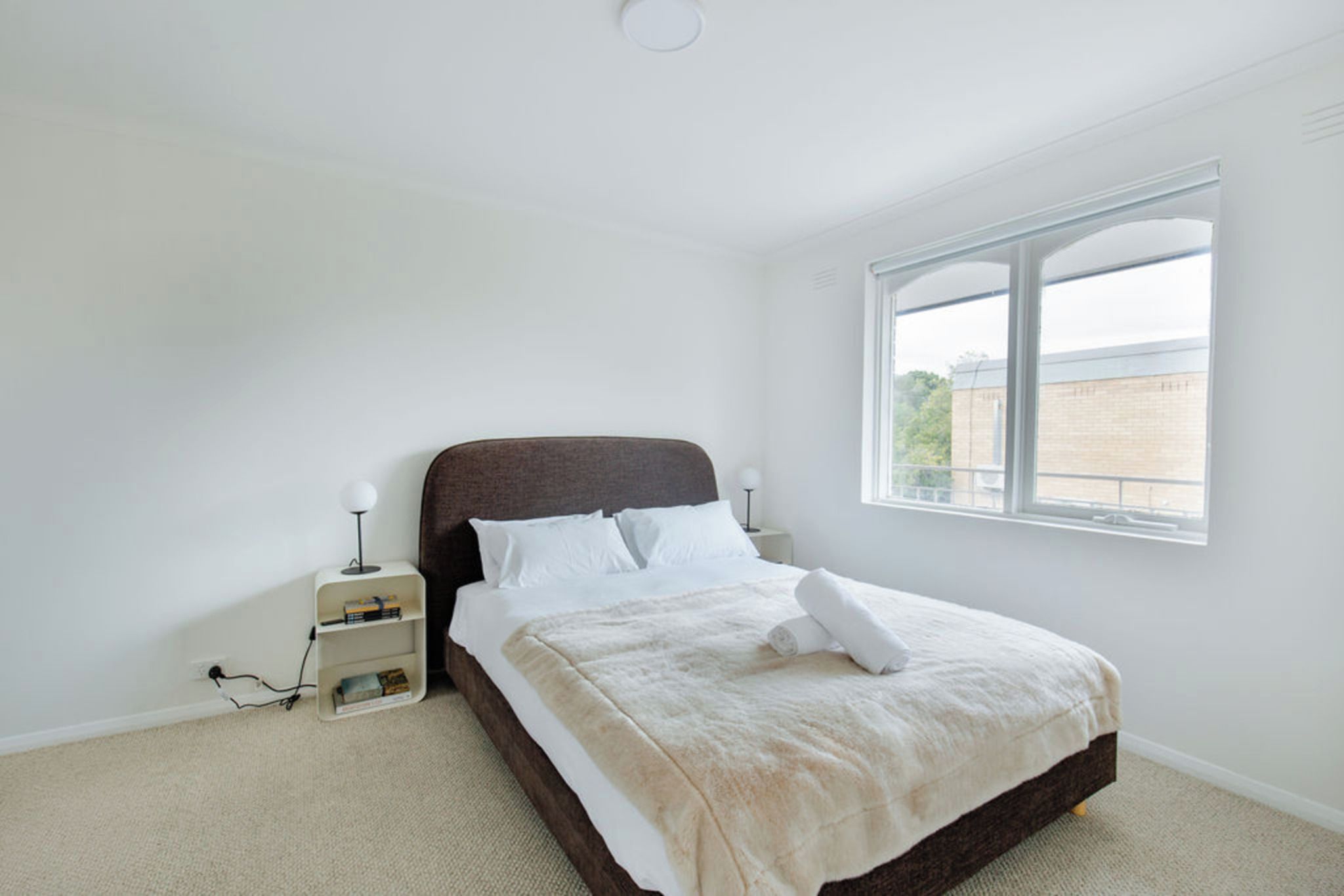 A bedroom with a bed, a nightstand, a lamp, and a window.