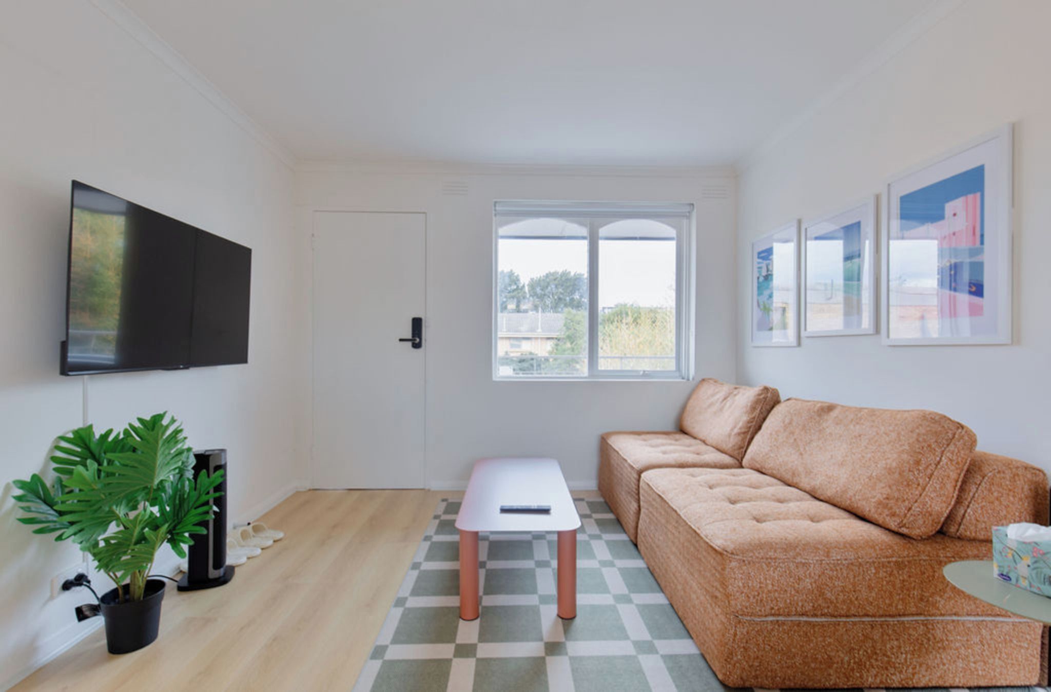Ein Wohnzimmer mit Sofa, einem kleinen Tisch, einem Fernseher, einem Fenster und einer Pflanze.