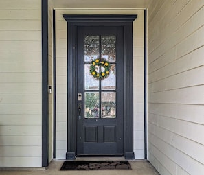 A dark gray front door with a glass panel, a wreath with yellow flowers, and a doormat with the word 'Welcome'. - The Cowboy Capital Escape: Resort-Style Backyard Pool & Outdoor Living. (Bandera)