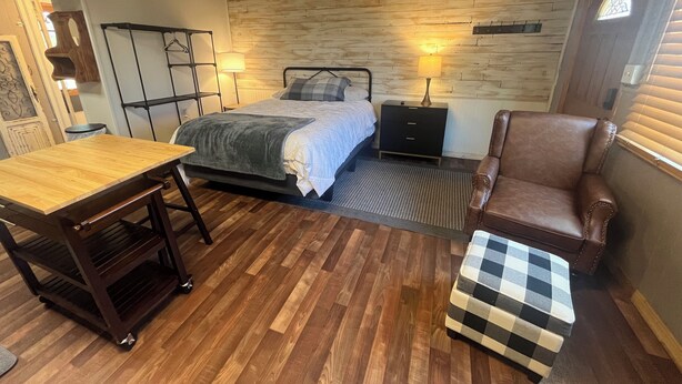 A room with a bed, a chair, a table, and a small ottoman. - Le Maison Bruin  (Cortez)