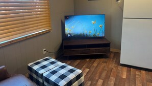 A room with a television on a wooden stand, a refrigerator, and a bench with a checkered cushion. - Le Maison Bruin  (Cortez)