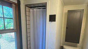 A small bathroom with a shower, toilet, and a window. - Le Maison Bruin  (Cortez)