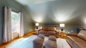 A cozy living room with a brown leather sofa, two side tables with lamps, a patterned rug, and a window with curtains. - Great for gatherings, hot tub, sauna, gas grill, firepit, gameroom, outdoor seating (Leicester)