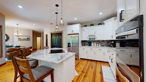A modern kitchen with a central island, white cabinetry, stainless steel appliances, and wooden flooring. - Great for gatherings, hot tub, sauna, gas grill, firepit, gameroom, outdoor seating (Leicester)
