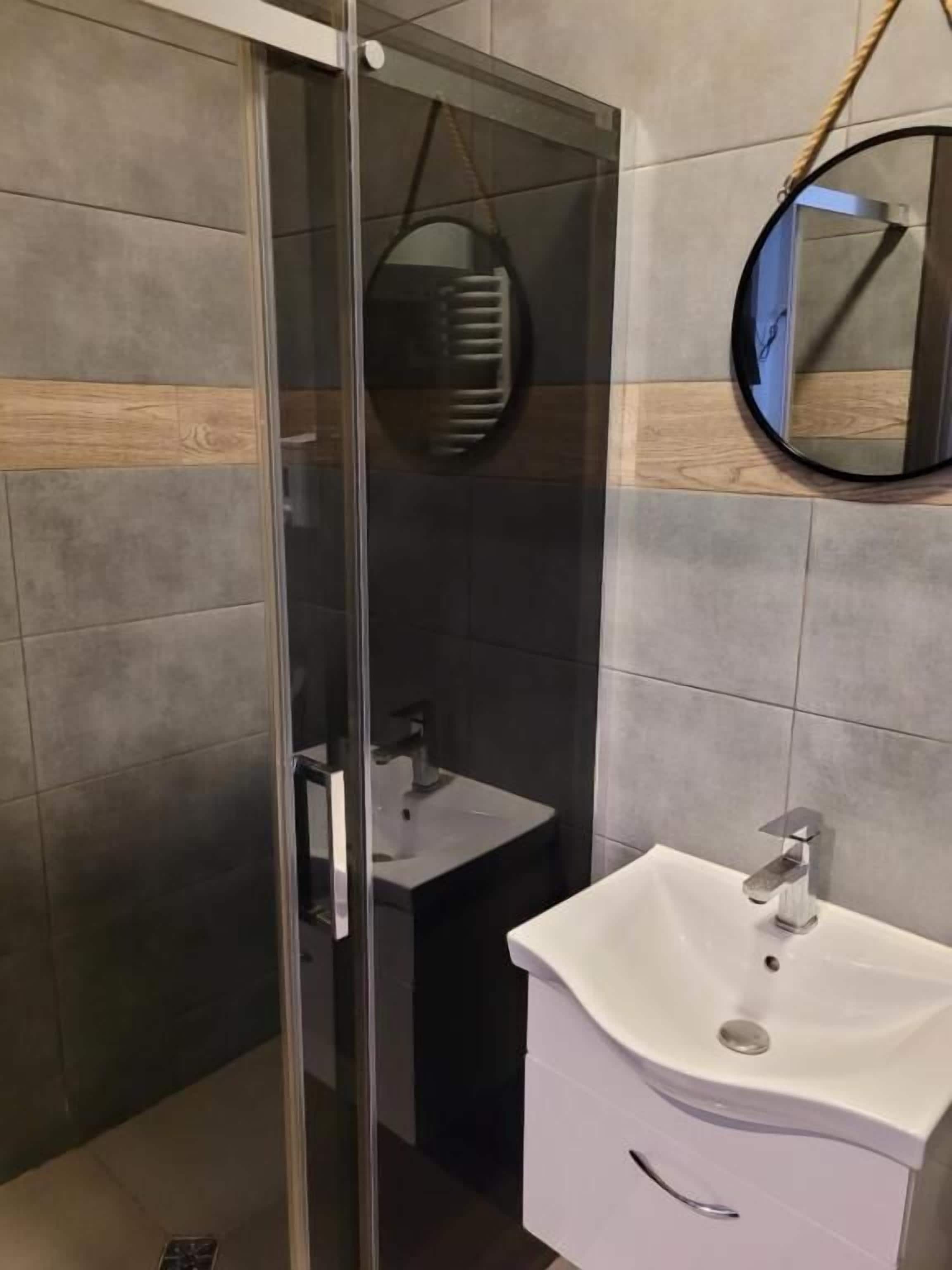 Un baño moderno con cabina de ducha de vidrio, un lavamanos blanco y un espejo.
