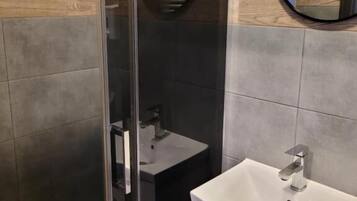 Un baño moderno con cabina de ducha de vidrio, un lavamanos blanco y un espejo.