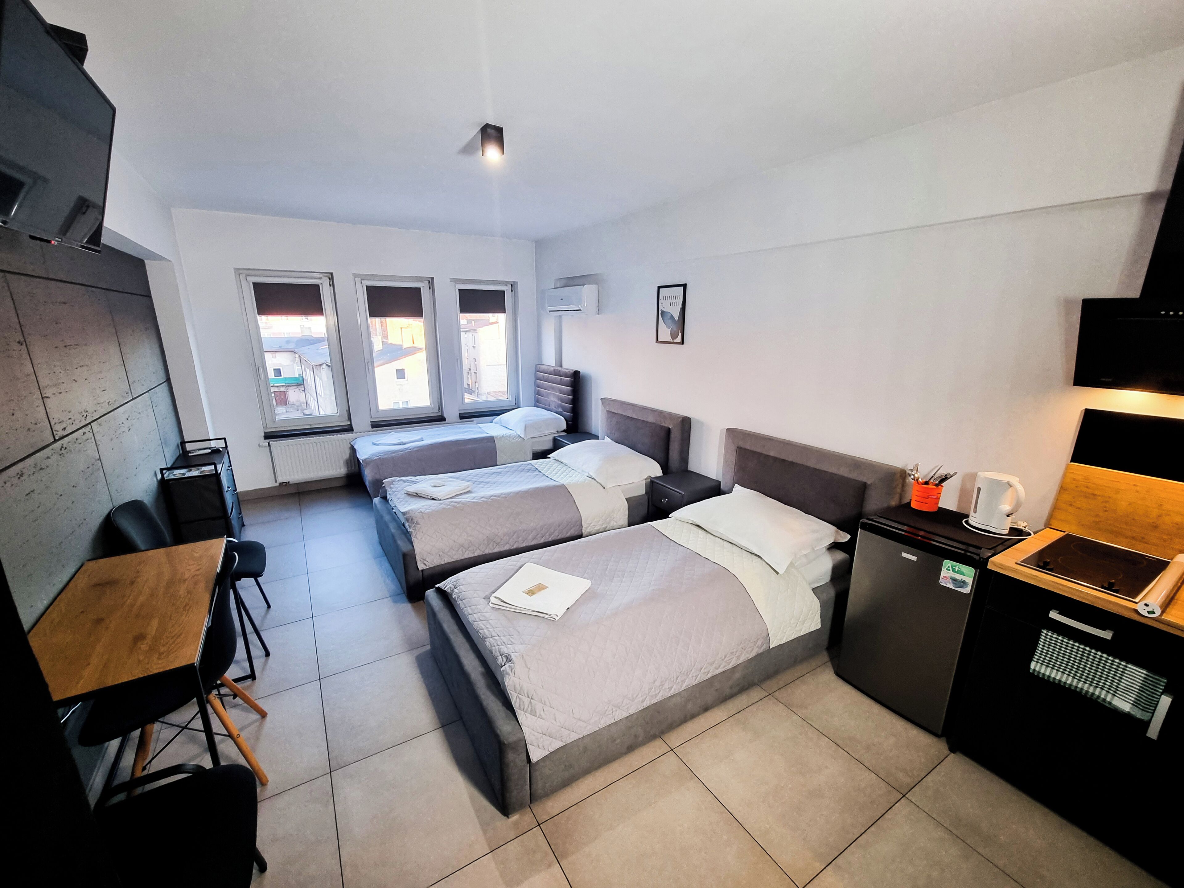 Habitación de hotel con dos camas, un escritorio, una silla, un televisor y una kitchenette.