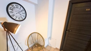 Una habitación con un reloj de pared, una lámpara de pie, una silla de mimbre y una puerta.