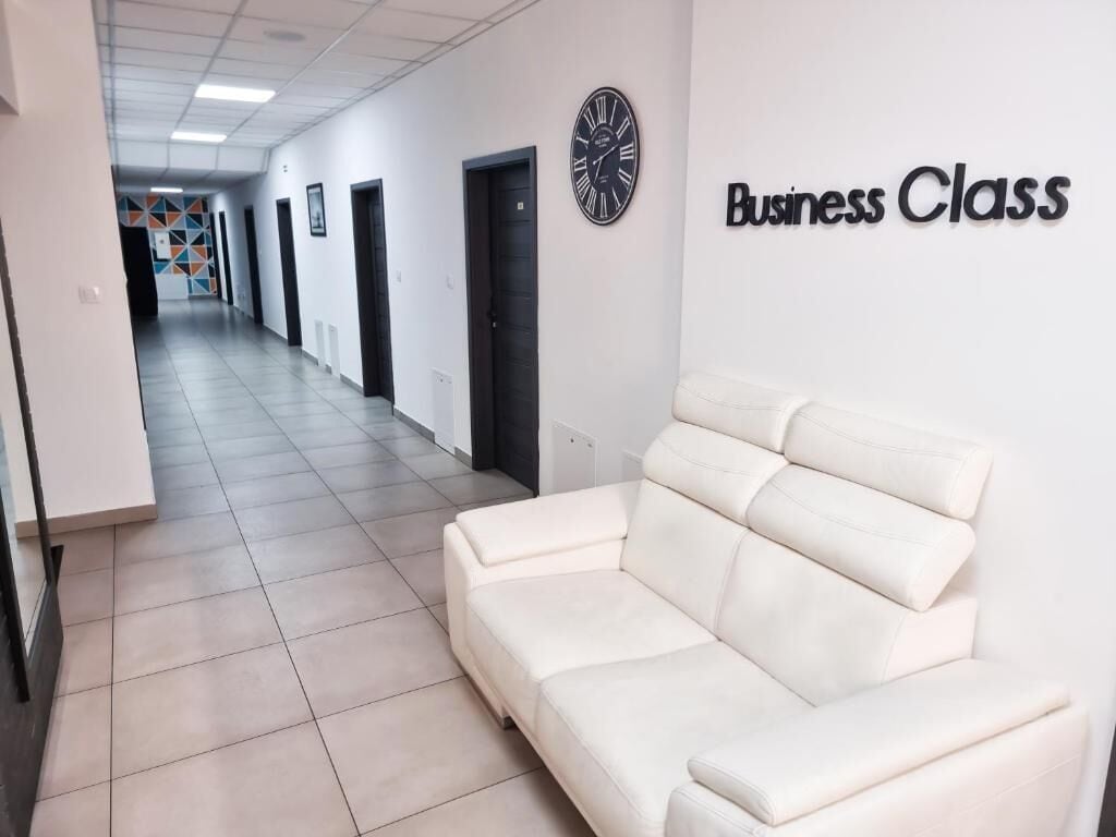 A hallway with a white couch, a clock, and a sign that reads 'Business Class'.