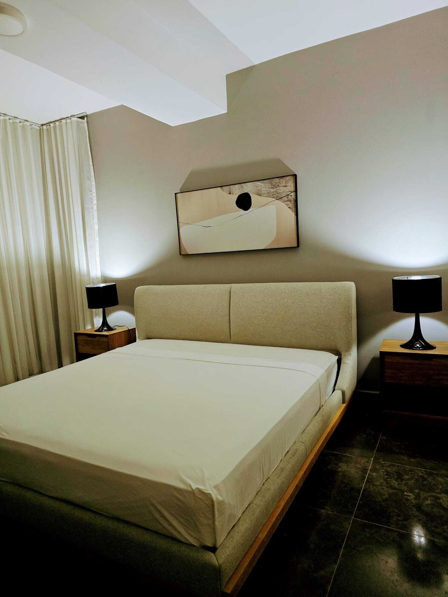 Ein Hotelzimmer mit einem großen Bett, zwei Nachttischen, einem Wandbild und einem Vorhang.