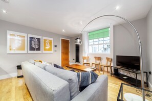 A modern living room with a sofa, a dining table, and a TV. - Host My Nest - Modern 2 Bed Apartment by Hyde Park (London)
