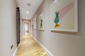 Un couloir doté d’un plancher en bois, de murs blancs et d’œuvres d’art encadrées.
