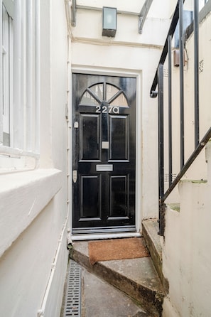 A black door with a numeric address, a metal handrail, and a small step leading to the entrance. - Host My Nest - Modern 2 Bed Apartment by Hyde Park (London)