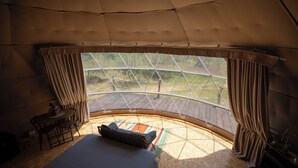 Un hébergement sous tente comprenant un lit, une petite table et une vue sur l’extérieur.