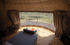 A tented accommodation with a bed, a small table, and a view of the outdoors.