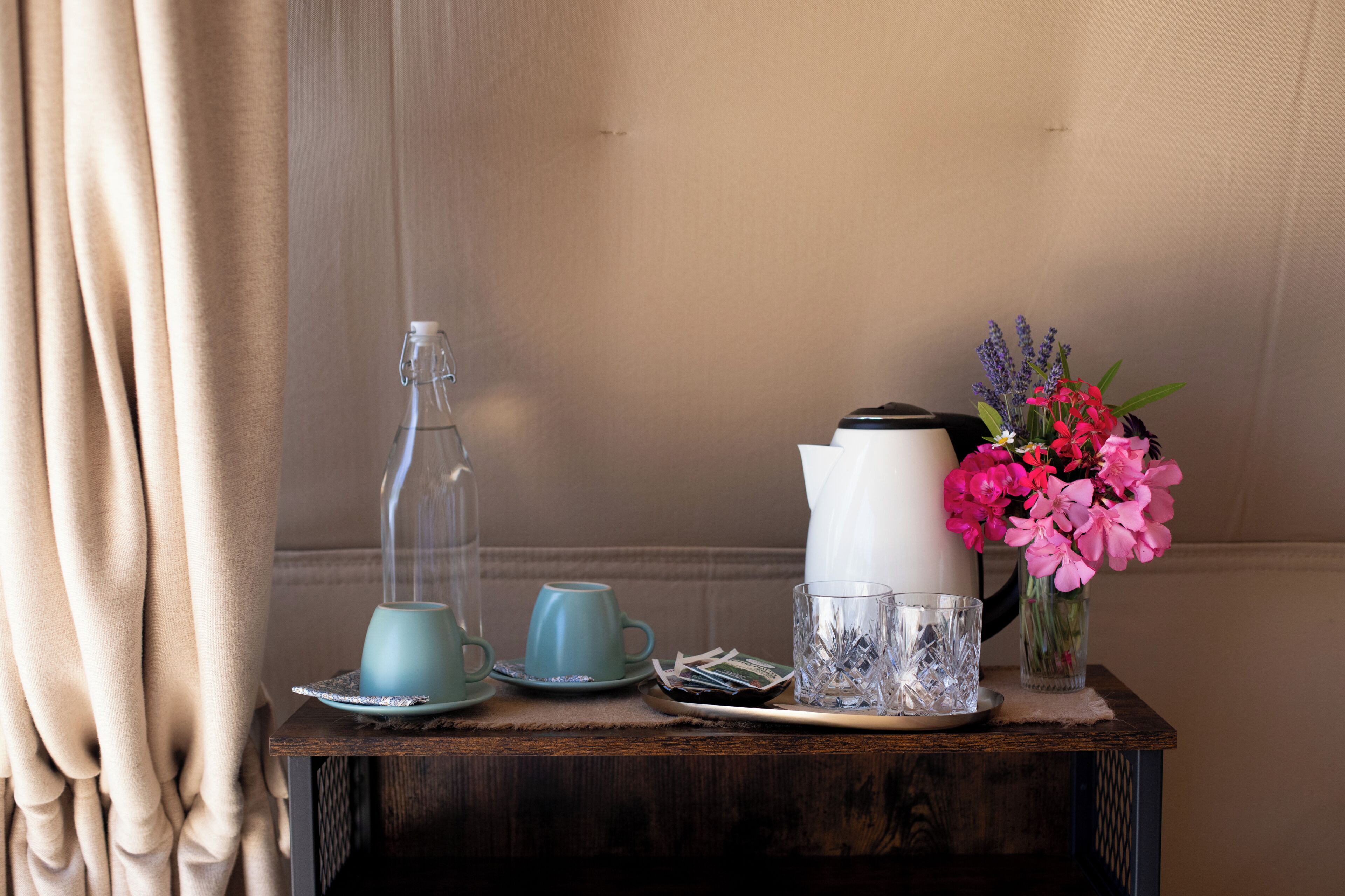 Una mesa de madera con una tetera, dos tazas, un vaso y un florero con flores.