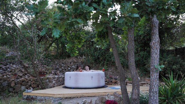 Un jardin avec un mur en pierre, une terrasse en bois et une grande structure gonflable.