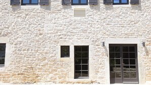 A two-story building with a stone facade and multiple windows with shutters.