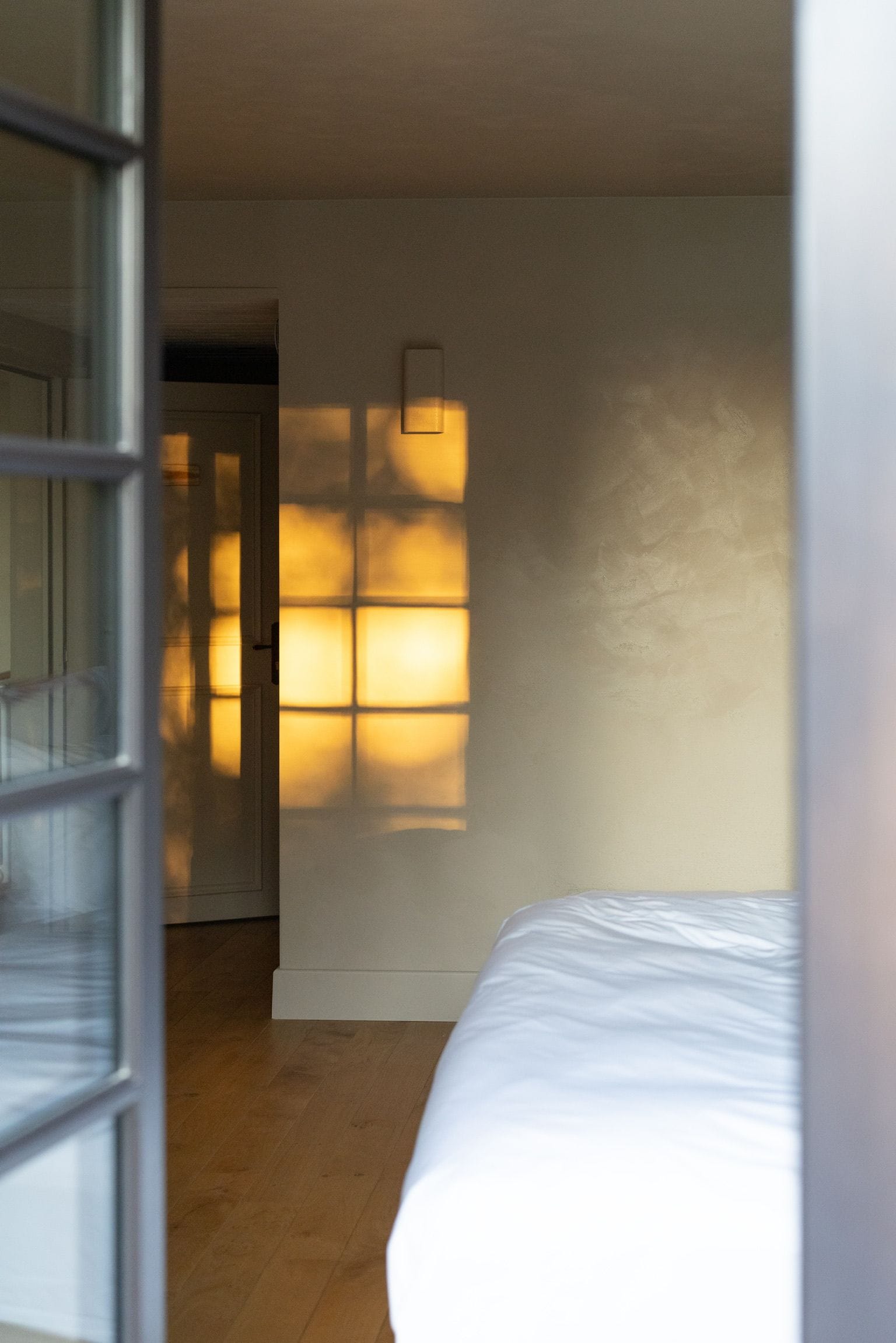 A bedroom with a bed, a door, and a wall with a light fixture.