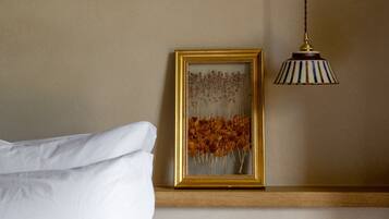 Une chambre à coucher avec un lit, un tableau encadré posé sur une étagère et une lampe suspendue.