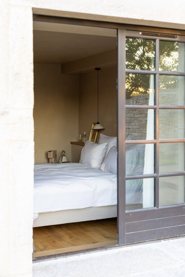 A bedroom with a bed, a kettle, and a window with a view of trees.