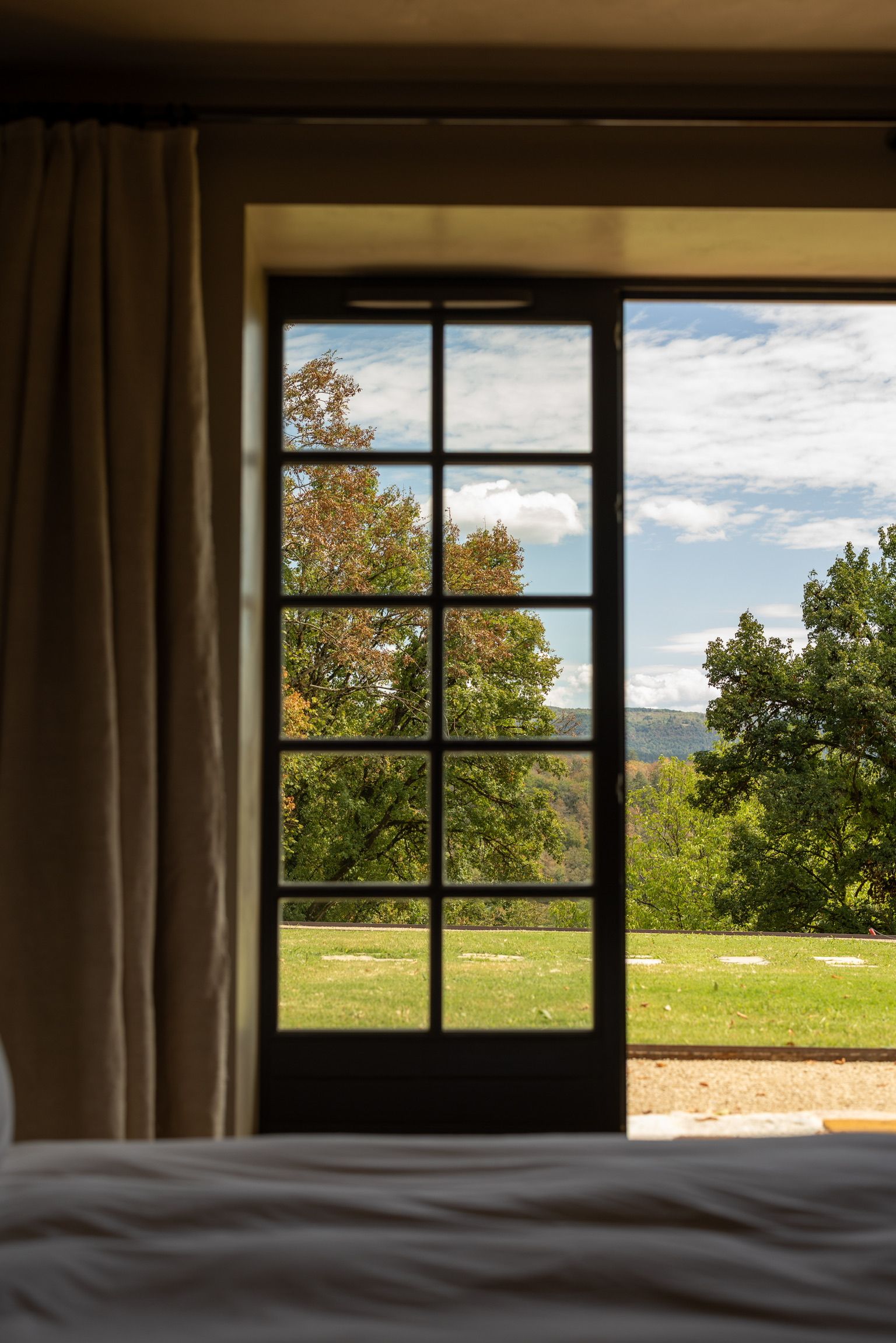 A room with a large window offering a view of a grassy field and trees.