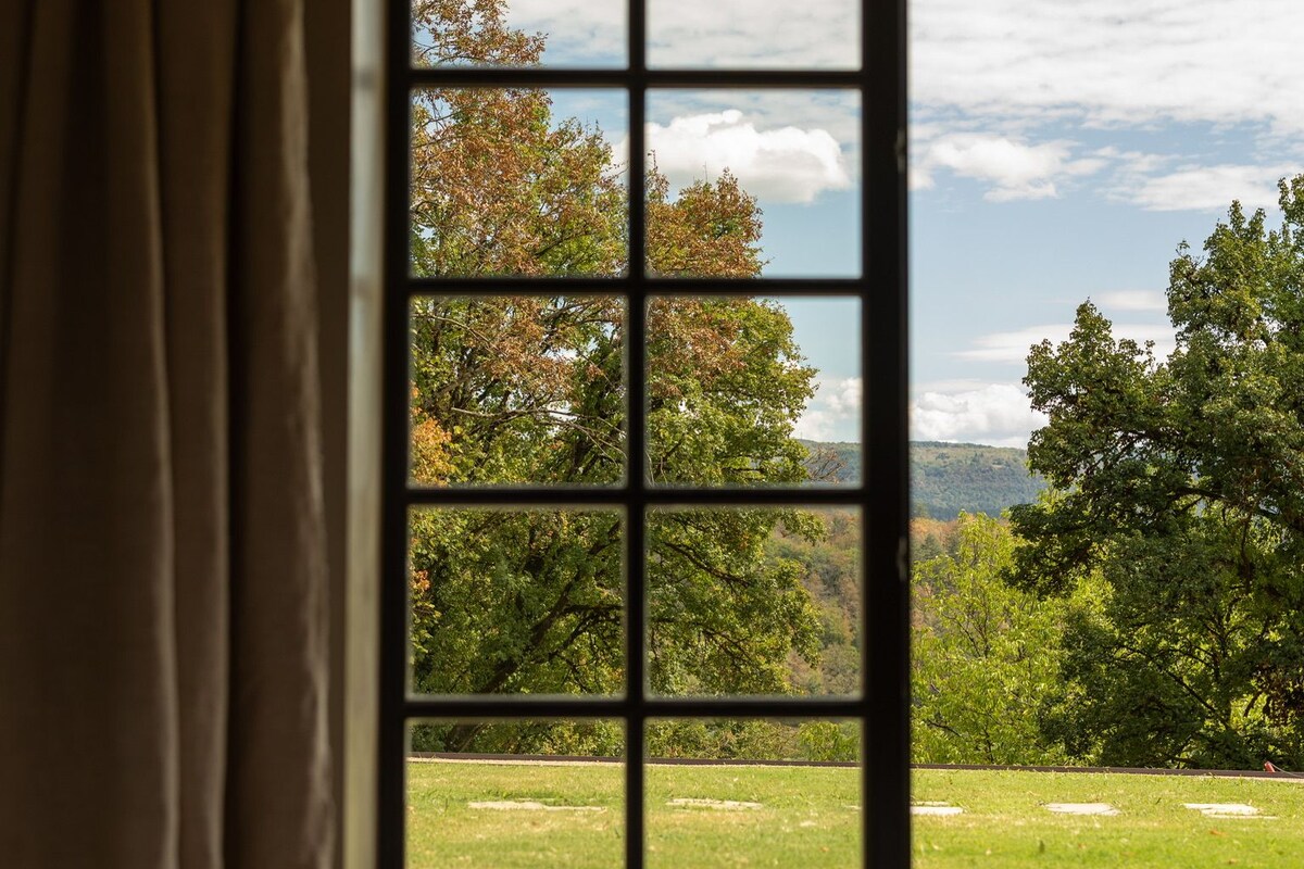 A room with a large window offering a view of a grassy field and trees.