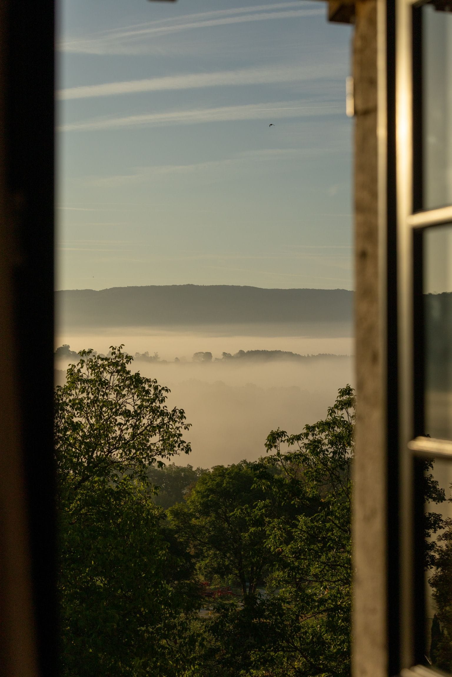 Uitzicht door een raam, met een heldere lucht, een verafgelegen bergketen en een laag mist of nevel.