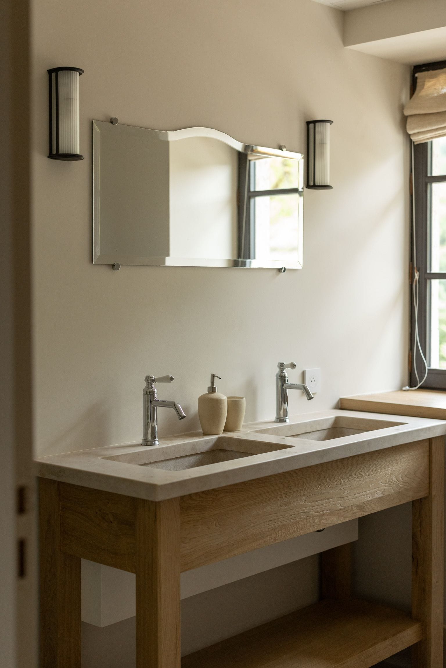 Baño con lavamanos doble, tocador de madera e iluminación en la pared.