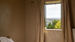 A bedroom with a single bed, a window with curtains, and a view of trees and hills. - AUBERGE DE MARIGNA (Marigna-sur-Valouse)